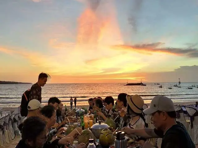 Travellers sharing a table on the sand as the sun goes down